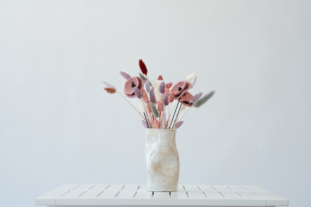 Ein Blumenarrangement in einer handgefertigten Keramikvase auf einem hellen Holztisch